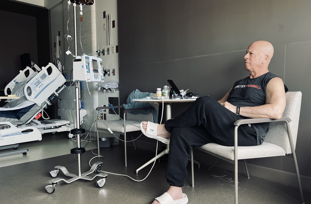 Howard Aaron sits in an armchair in his patient room, next to an IV pole. 